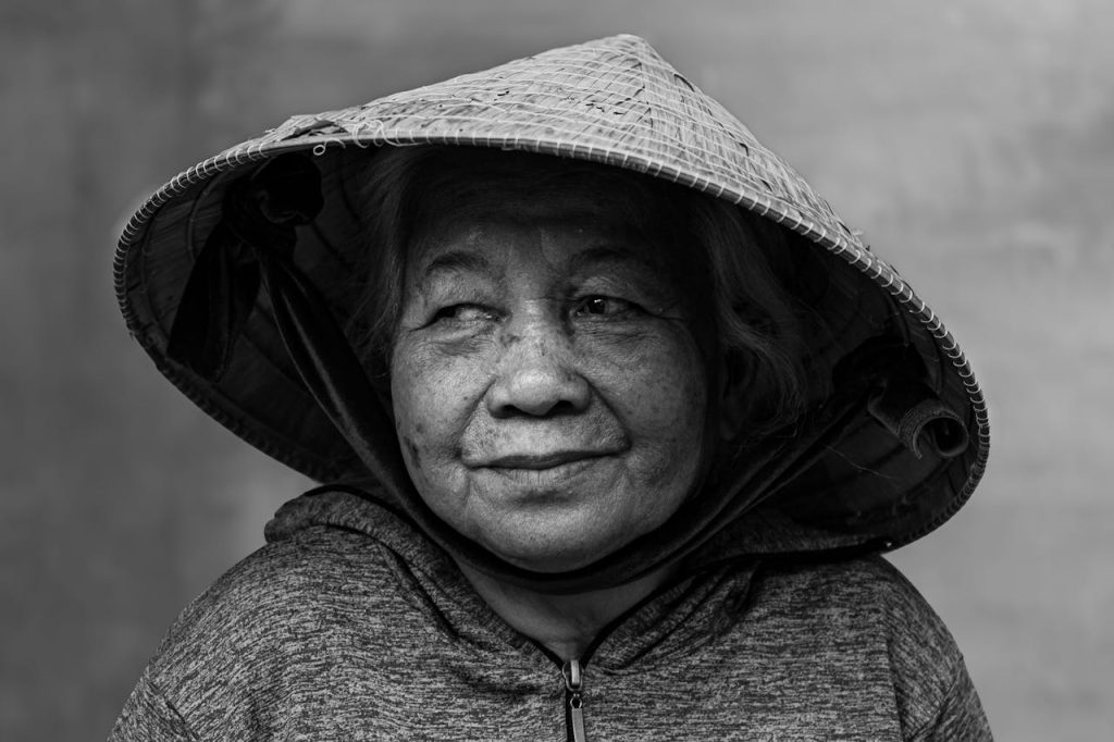 Black and white portrait of an elderly Vietnamese woman wearing a conical hat, showcasing cultural heritage.